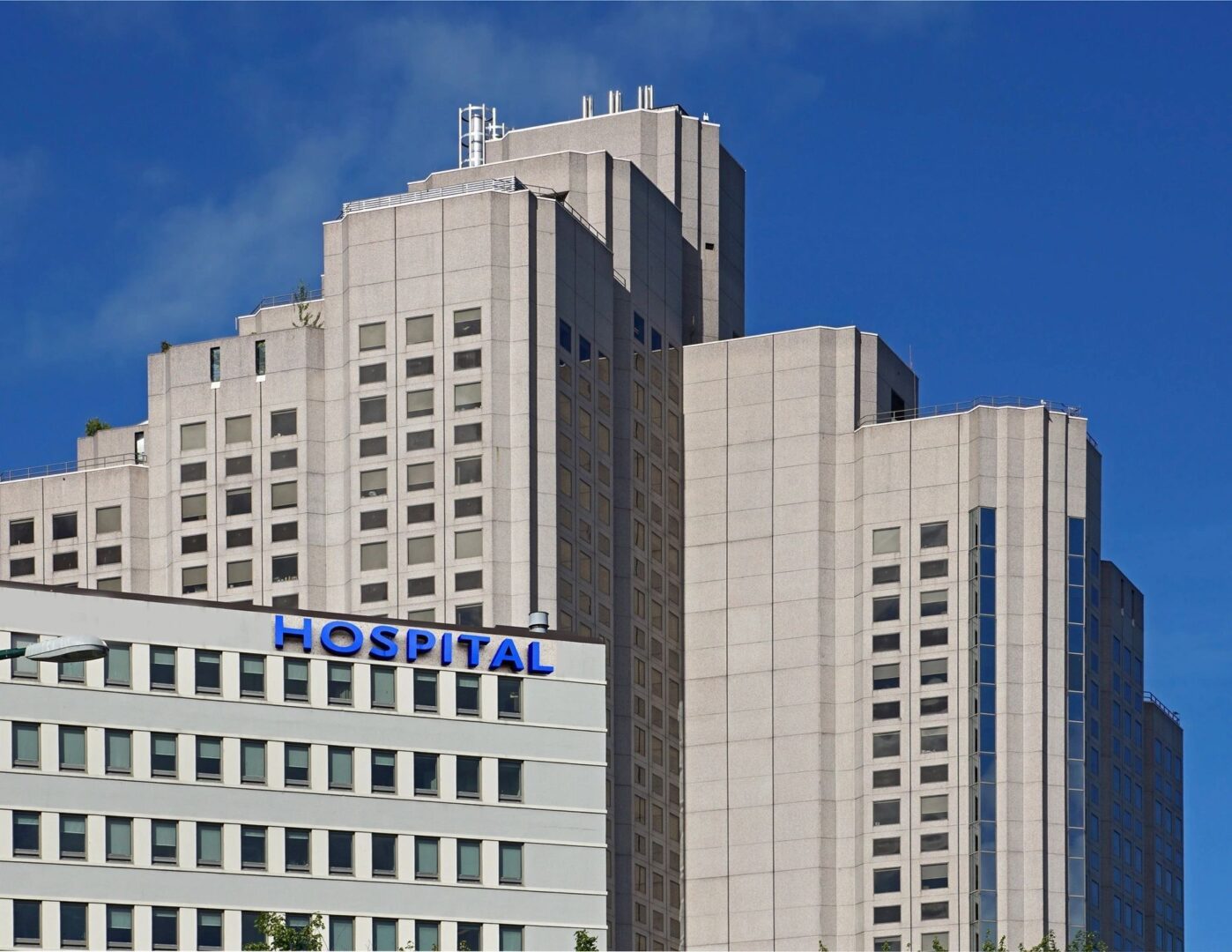 A large building with many windows and a blue hospital sign.